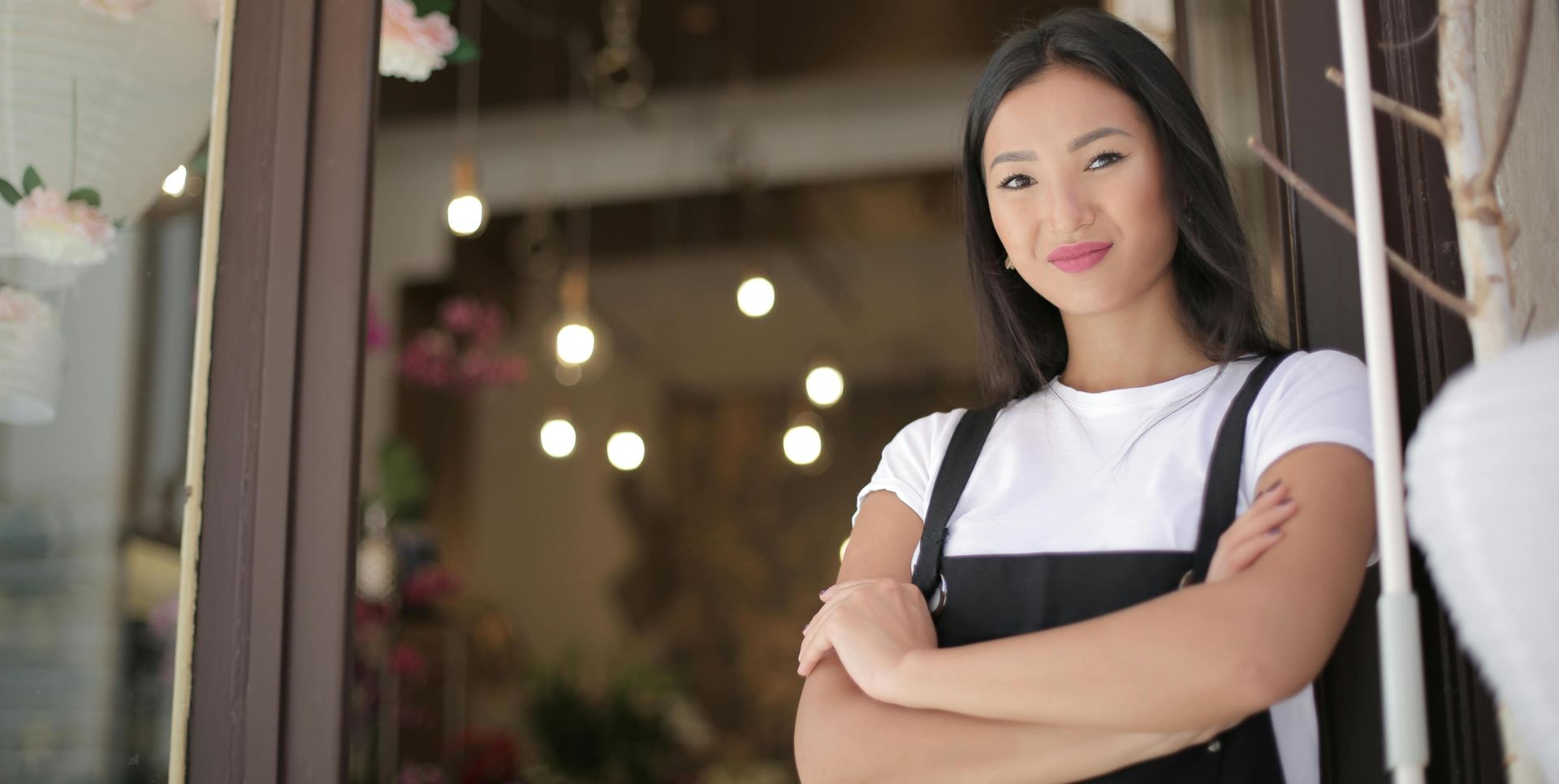 Smiling female florist standing with arms crossed at shop entrance, exuding confidence and friendliness.