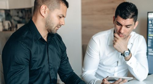 Two businessmen discussing stock market analytics in a modern office setting.