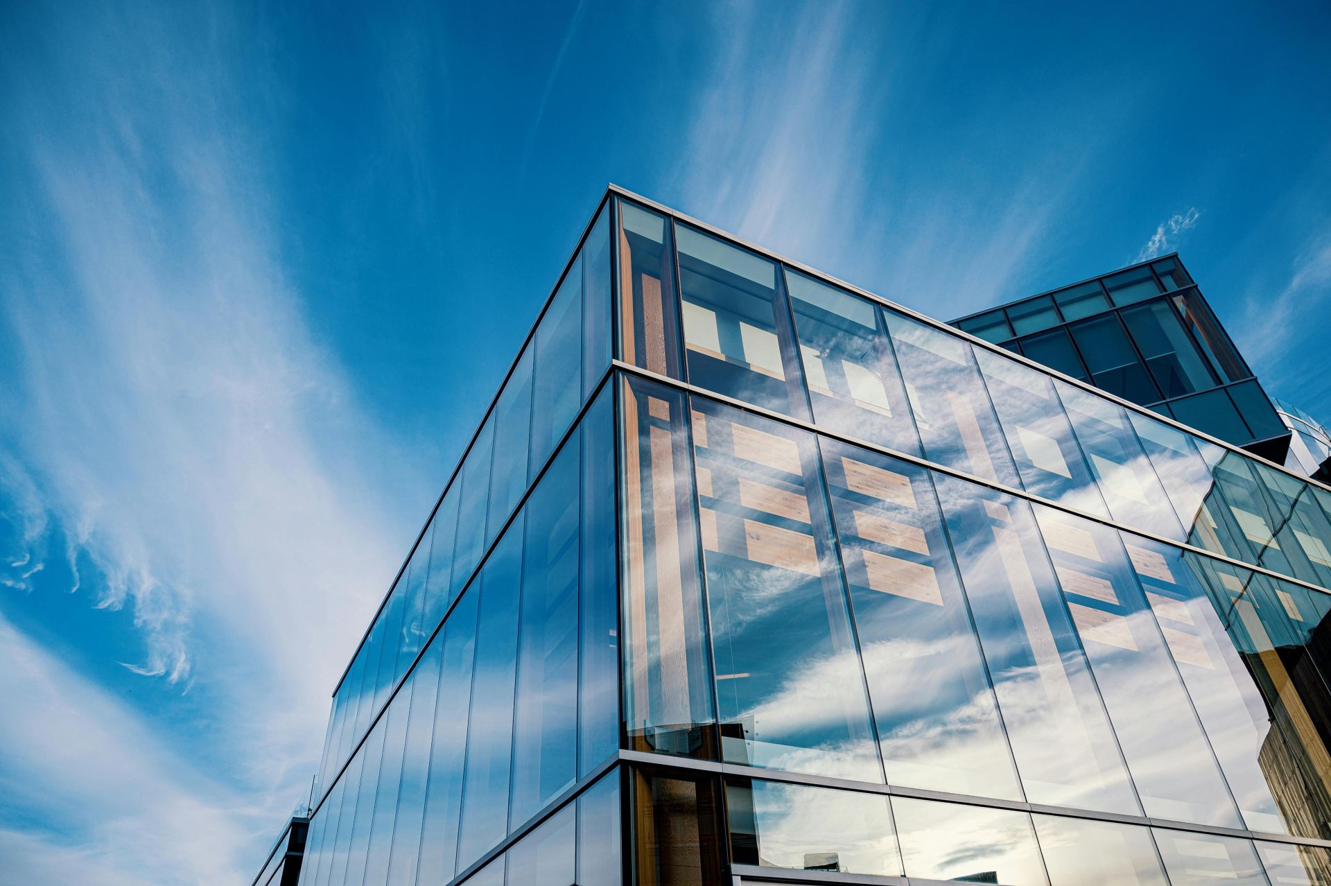 Sleek glass facade reflecting clouds in a modern architectural design under a bright blue sky.