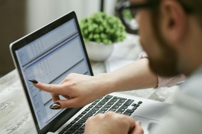 Two people working on a laptop analyzing data, pointing at screen.