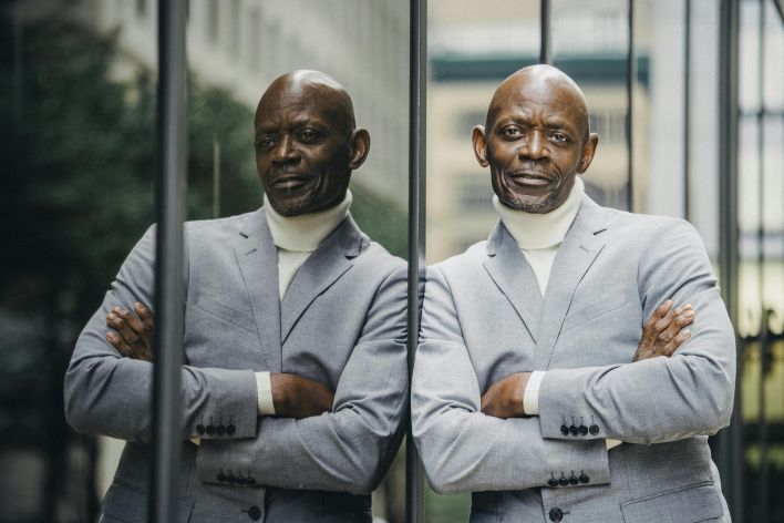 Charismatic black businessman in a suit standing with arms crossed outdoors.